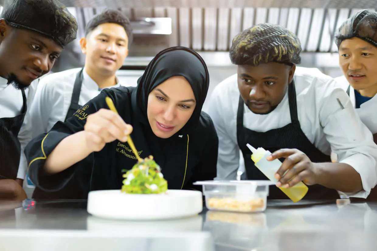 Chef Mariam plating a dish as two young chefs watch