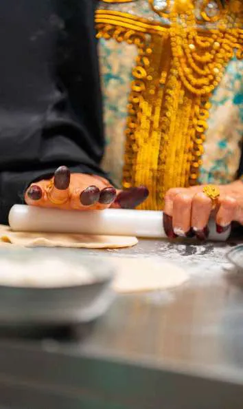Hands with henna rolling dough with a wooden pin