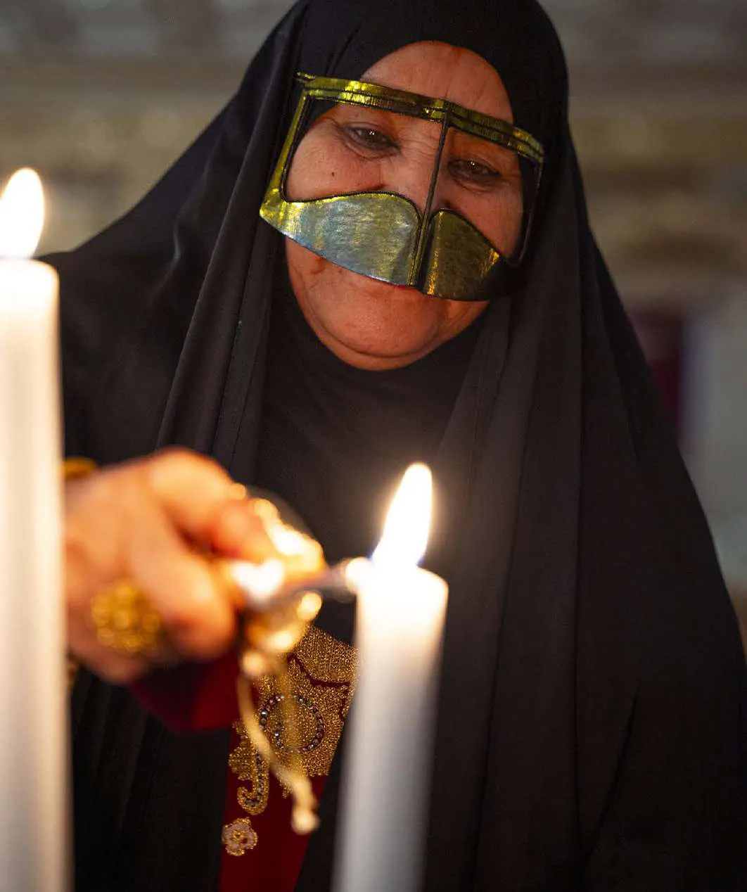 Amina lighting a candle, the gold burqa catching the light