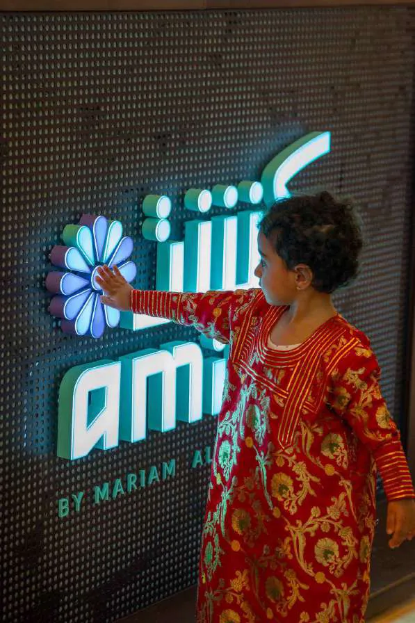 A child reaching for the neon Amina sign